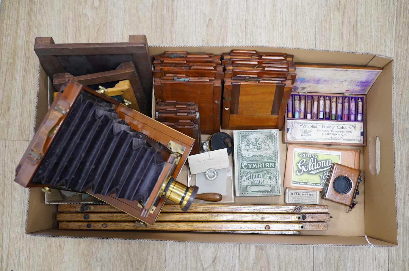 A late 19th century brass and mahogany half plate bellows camera with oak tripod stand and a lens engraved ‘ERR 6.5 x 4.75’, together with a good quantity of contemporary accessories including a shutter action, ten negat